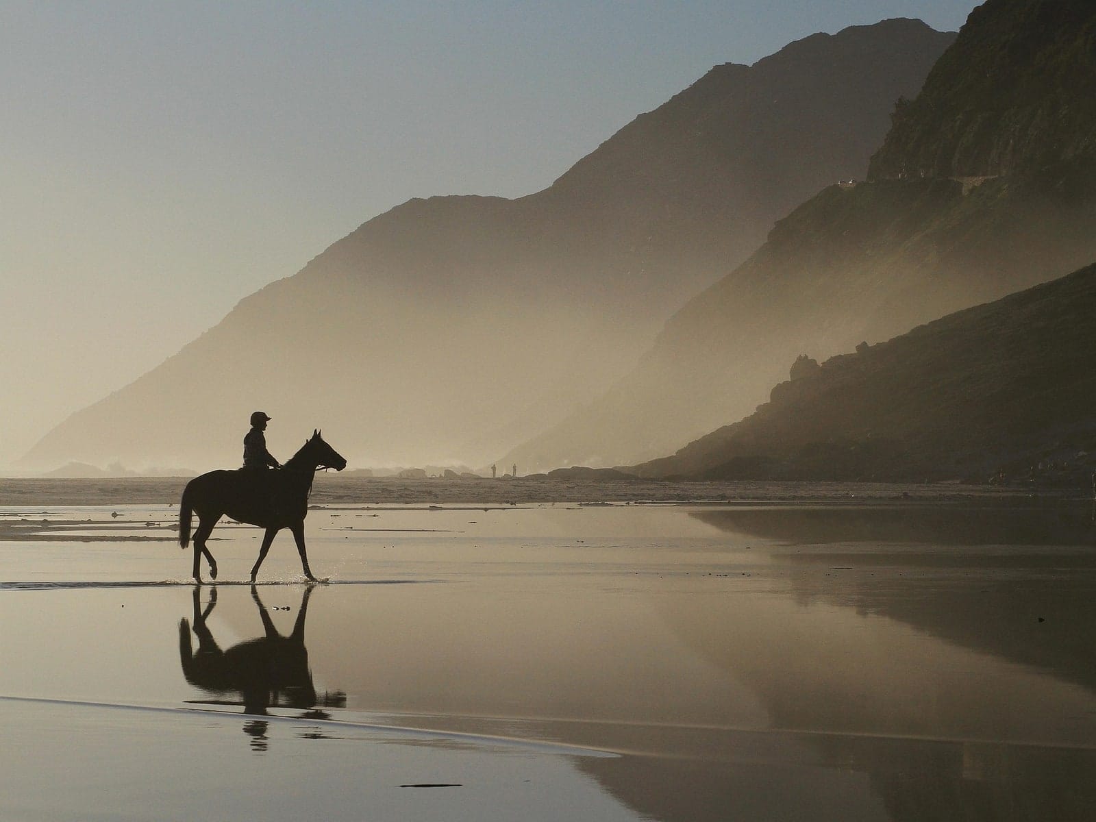 A lone rider on the wet sand at Noordhoek with Chapman's Peak behind