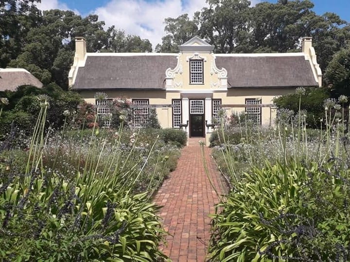A brick path through lavender and agapanthus to the gable of a Cape Dutch homestead