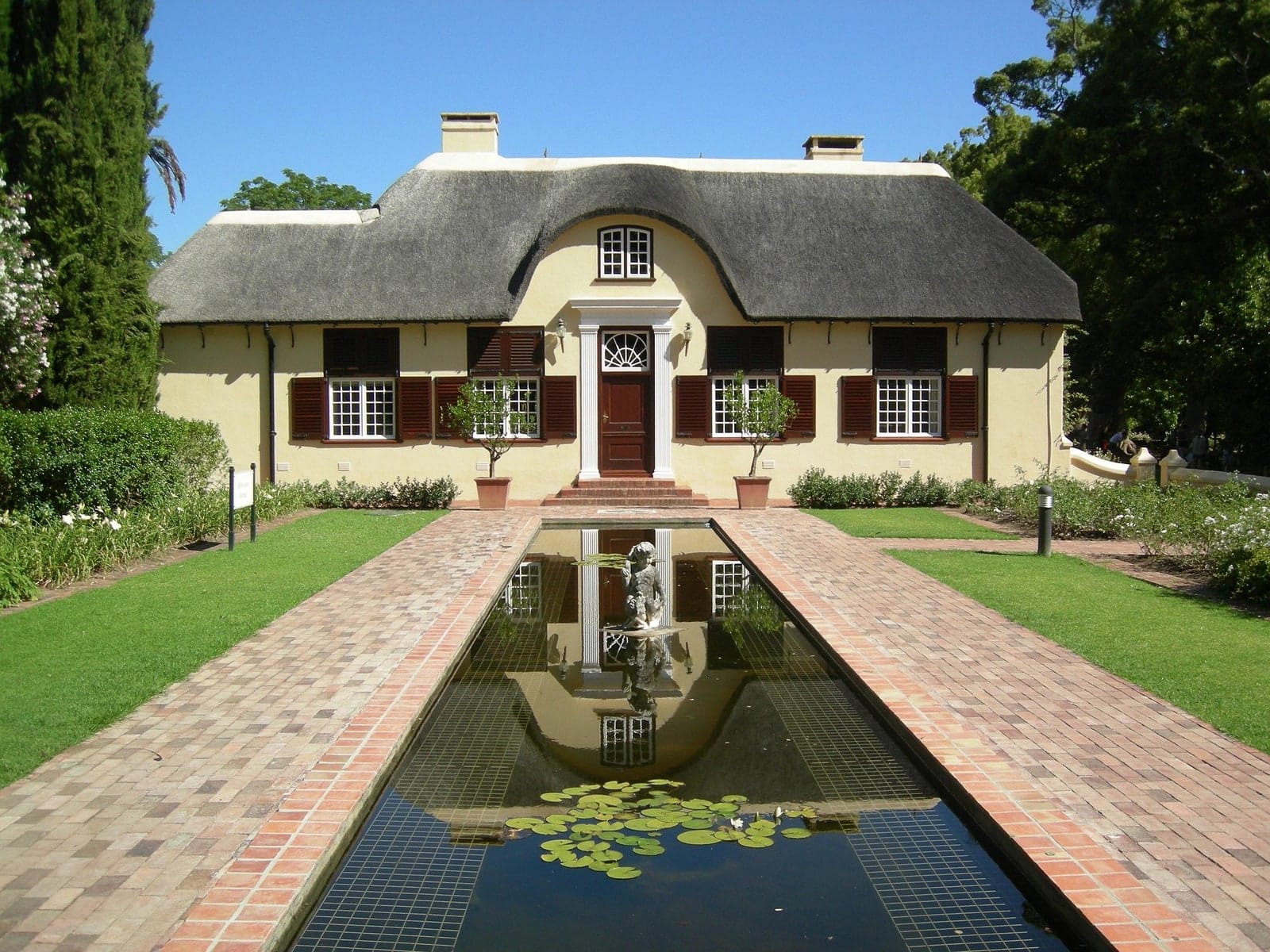 A thatched Cape Dutch homestead behind a long reflecting pool and lawns