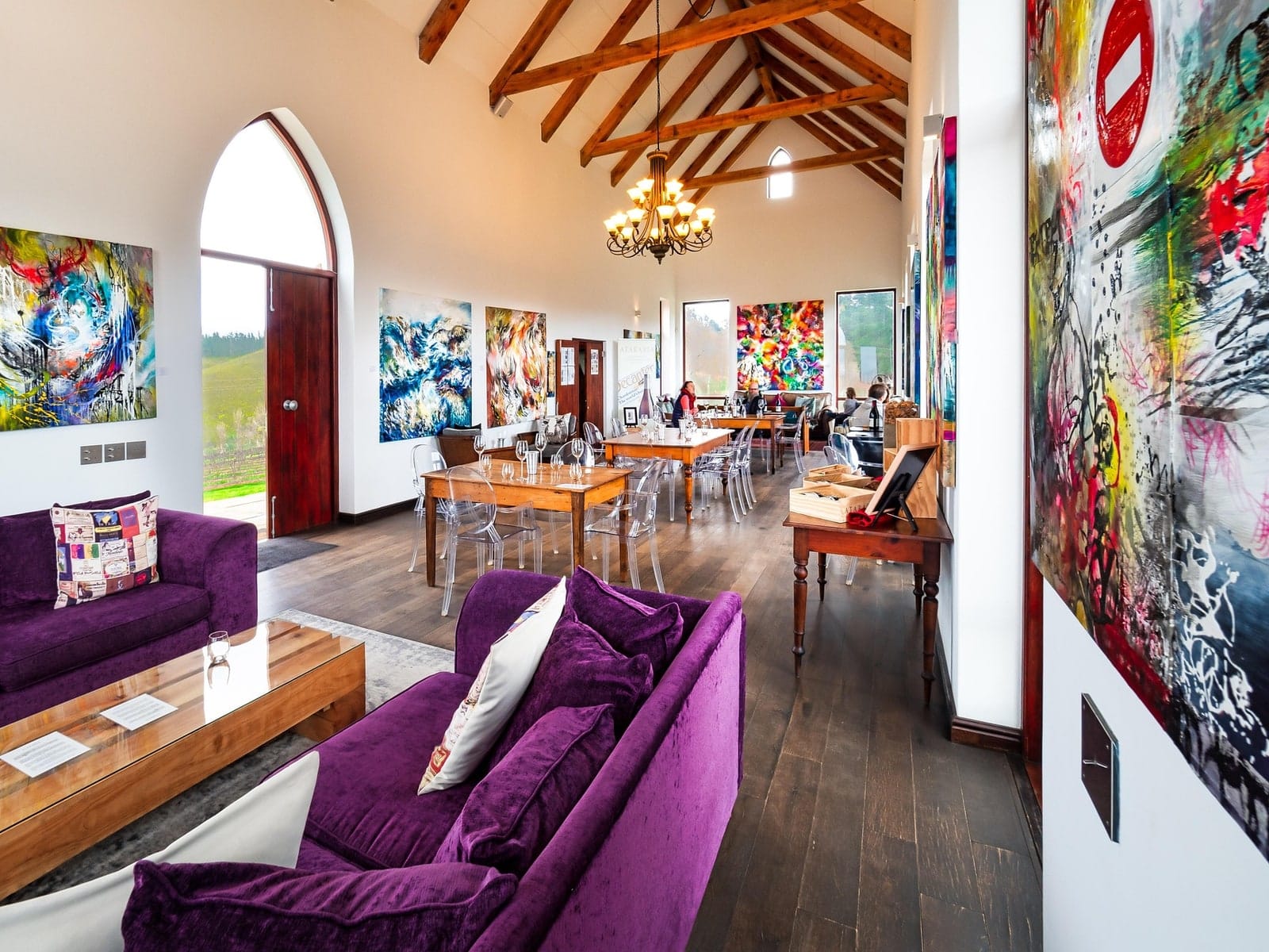A tasting room under a beamed roof, hung with large contemporary paintings