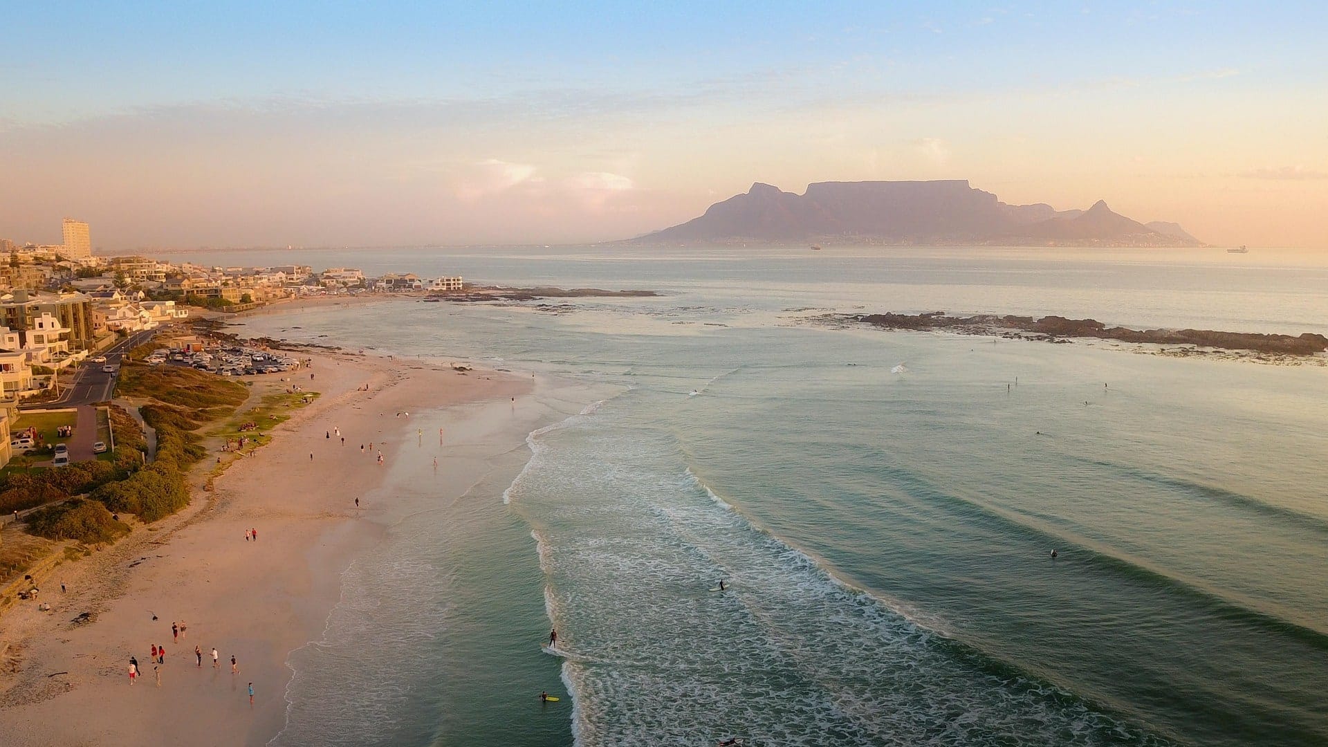 Surfers and a long beach at Blouberg with Table Mountain across the bay at sunset